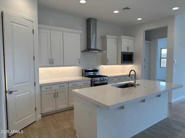 kitchen with stainless steel appliances, wall chimney exhaust hood, a sink, light wood-type flooring, and backsplash
