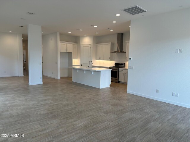 kitchen featuring stainless steel range with gas cooktop, wall chimney range hood, a sink, open floor plan, and recessed lighting