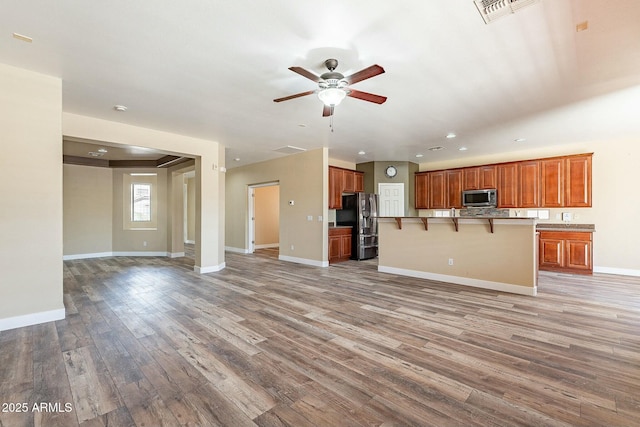 kitchen featuring light wood finished floors, stainless steel microwave, visible vents, open floor plan, and fridge with ice dispenser