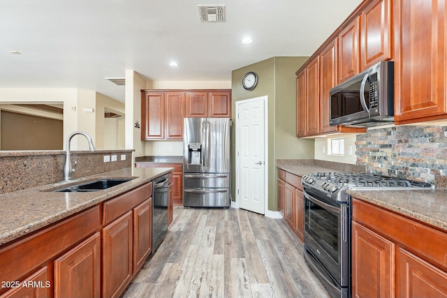 kitchen with light wood finished floors, appliances with stainless steel finishes, stone counters, and a sink