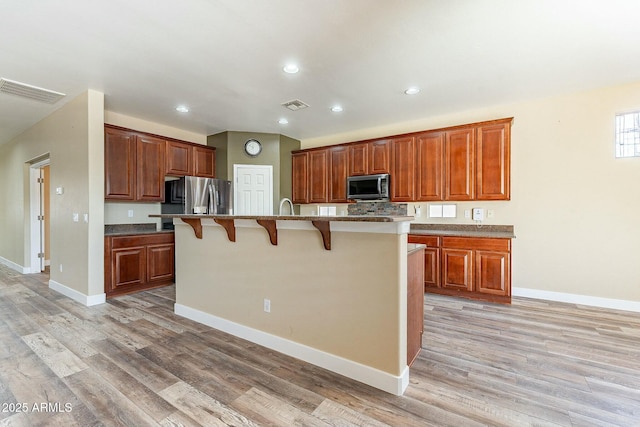 kitchen featuring appliances with stainless steel finishes, light wood-style flooring, a breakfast bar, and visible vents