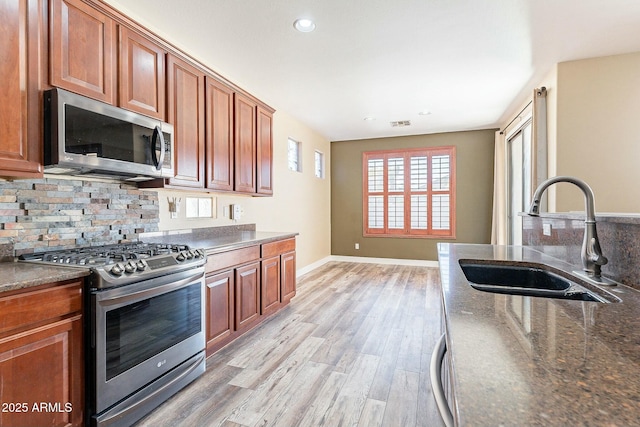 kitchen with light wood finished floors, brown cabinetry, a sink, stainless steel appliances, and backsplash