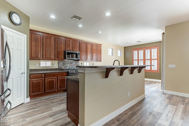 kitchen with stainless steel appliances, visible vents, light wood-style flooring, and a kitchen bar