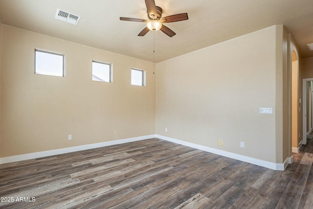 empty room with dark wood-style floors, baseboards, visible vents, and arched walkways