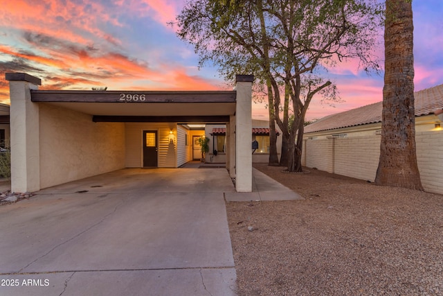 back of property at dusk featuring a carport, fence, driveway, and stucco siding