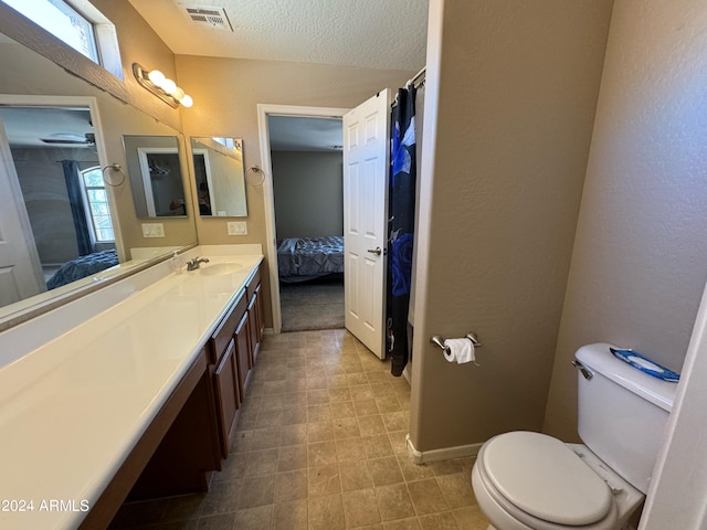 bathroom featuring vanity, a textured ceiling, a healthy amount of sunlight, and toilet