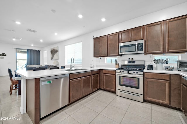 kitchen featuring sink, stainless steel appliances, kitchen peninsula, dark brown cabinets, and light tile patterned floors