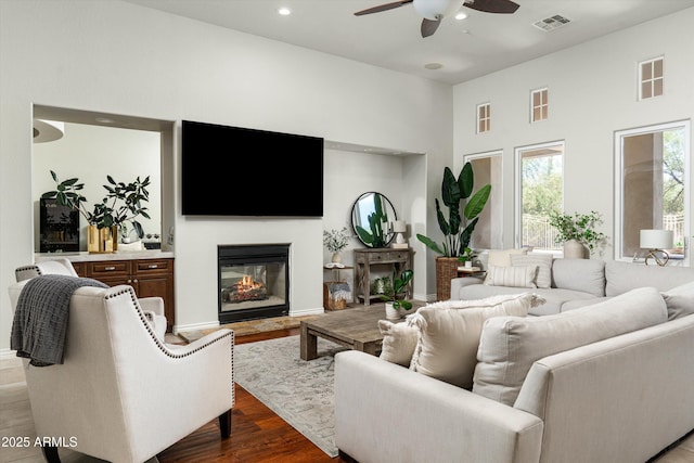 8240 E Wingspan Way, Scottsdale, AZ 85255 - living area featuring ceiling fan, a glass covered fireplace, recessed lighting, dark wood-type flooring, and a towering ceiling
