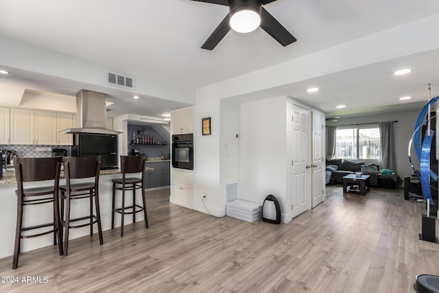 kitchen with a kitchen bar, light hardwood / wood-style flooring, island exhaust hood, oven, and decorative backsplash