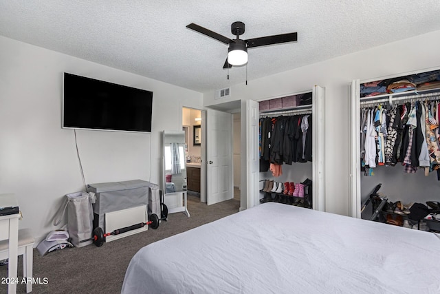 bedroom featuring ceiling fan, two closets, a textured ceiling, and dark carpet