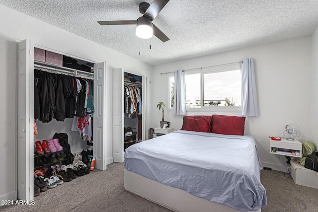 carpeted bedroom featuring ceiling fan, two closets, and a textured ceiling