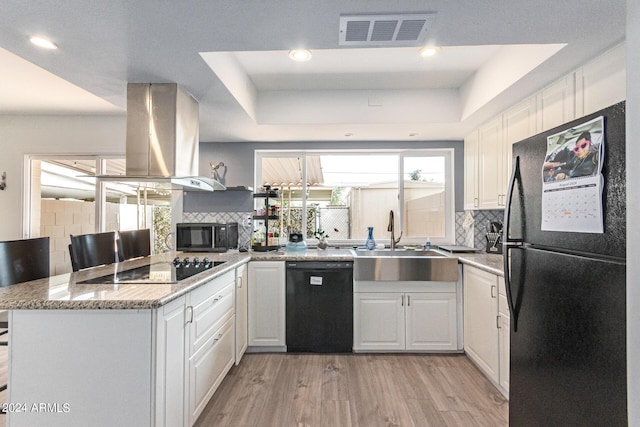 kitchen featuring white cabinetry, island range hood, kitchen peninsula, light stone countertops, and black appliances