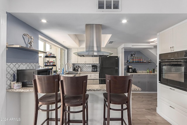 kitchen with white cabinetry, a breakfast bar area, decorative backsplash, island exhaust hood, and black appliances