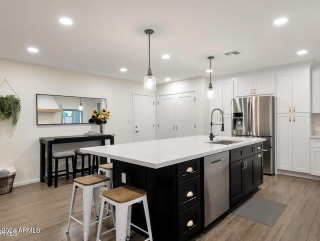 kitchen featuring stainless steel appliances, decorative light fixtures, light hardwood / wood-style flooring, white cabinetry, and an island with sink