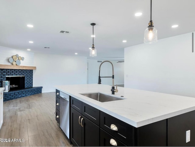 kitchen featuring pendant lighting, sink, a brick fireplace, light hardwood / wood-style flooring, and an island with sink