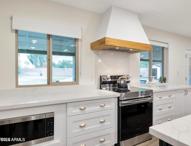 kitchen featuring light stone countertops, backsplash, custom range hood, stainless steel appliances, and light hardwood / wood-style floors