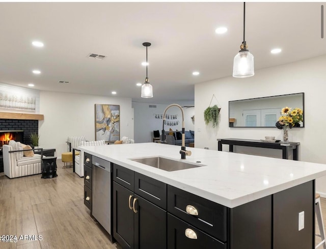 kitchen featuring light wood-type flooring, sink, a center island with sink, a fireplace, and hanging light fixtures