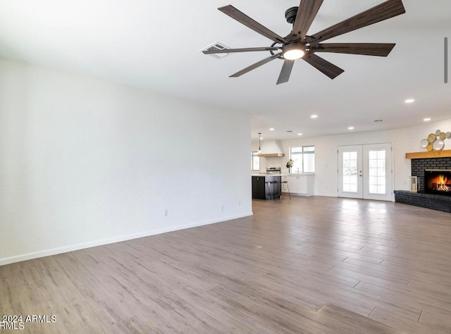 unfurnished living room featuring hardwood / wood-style flooring, a brick fireplace, and french doors