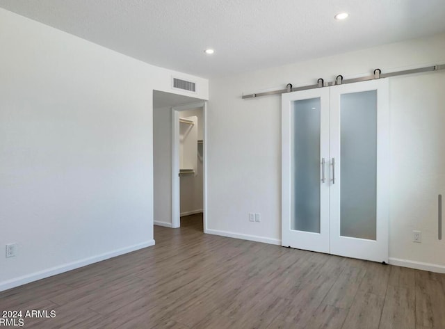 unfurnished room featuring a barn door, hardwood / wood-style floors, and a textured ceiling