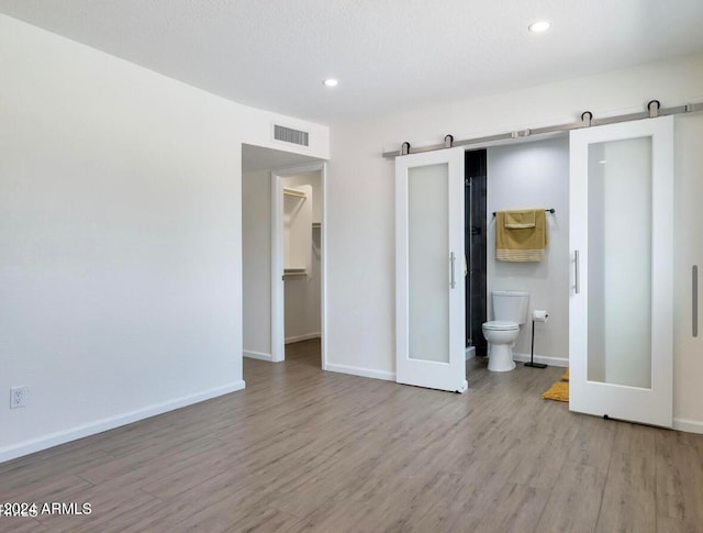 unfurnished bedroom featuring wood-type flooring, a barn door, a spacious closet, connected bathroom, and a closet