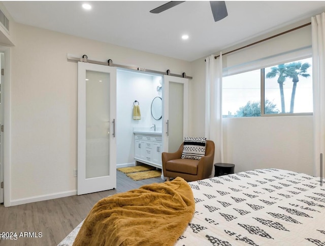 bedroom featuring light wood-type flooring, ensuite bath, ceiling fan, sink, and a barn door