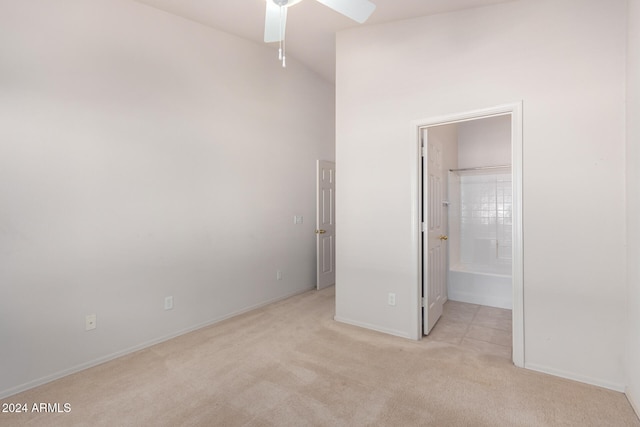 unfurnished bedroom with ensuite bathroom, light colored carpet, ceiling fan, and a high ceiling