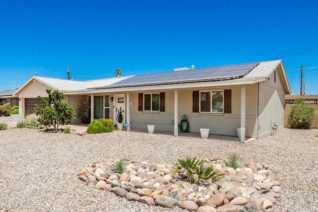 ranch-style house with a garage, a porch, and solar panels