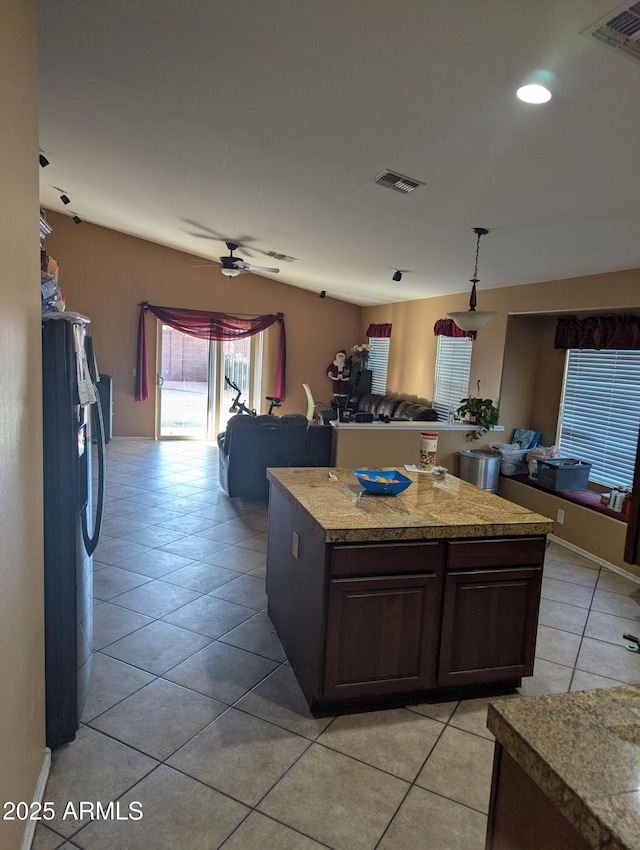 kitchen featuring light tile patterned flooring, a kitchen island, ceiling fan, dark brown cabinetry, and black fridge