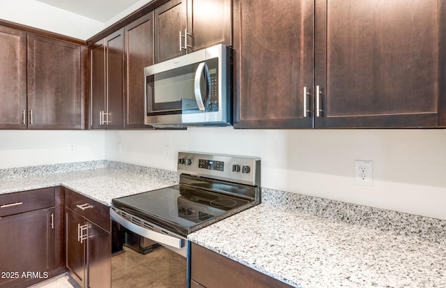 kitchen with appliances with stainless steel finishes, tile patterned flooring, light stone counters, and dark brown cabinetry