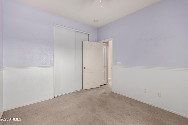 unfurnished bedroom featuring ceiling fan, a closet, and light colored carpet