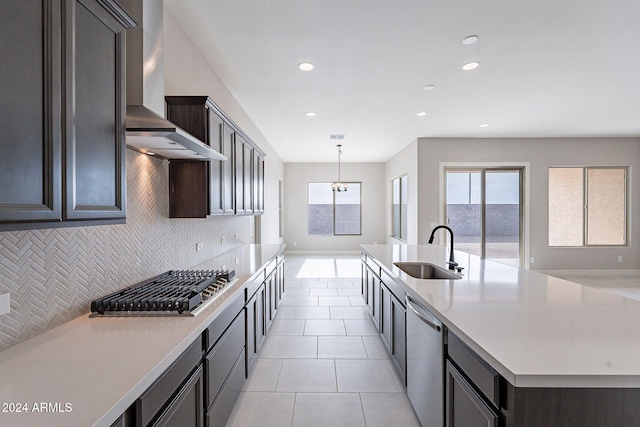 kitchen featuring sink, wall chimney exhaust hood, backsplash, a center island with sink, and appliances with stainless steel finishes