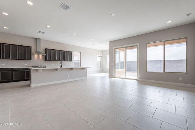 kitchen with wall chimney exhaust hood, light tile patterned floors, backsplash, and a kitchen island with sink