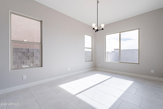 tiled spare room featuring a notable chandelier