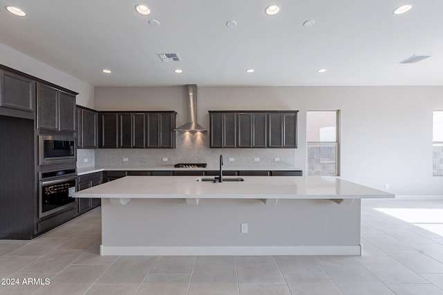 kitchen with wall chimney range hood, appliances with stainless steel finishes, a center island with sink, and sink