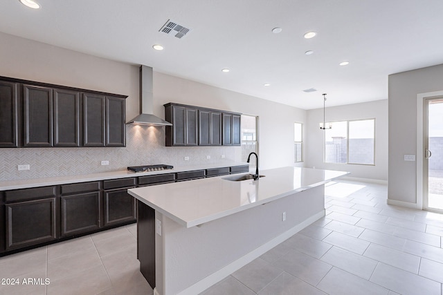 kitchen featuring sink, wall chimney exhaust hood, a kitchen island with sink, stainless steel gas stovetop, and decorative backsplash