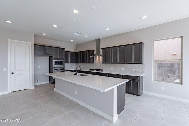 kitchen featuring sink, wall chimney exhaust hood, backsplash, an island with sink, and appliances with stainless steel finishes