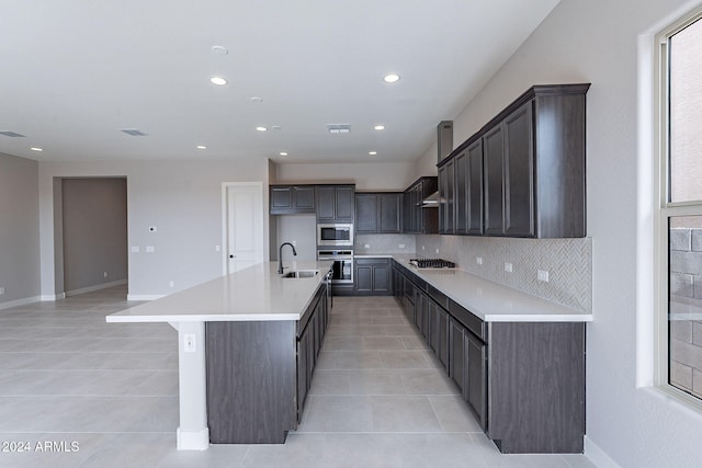 kitchen with decorative backsplash, a kitchen island with sink, light tile patterned floors, and stainless steel appliances