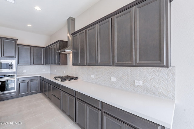 kitchen featuring backsplash, wall chimney exhaust hood, light tile patterned floors, dark brown cabinetry, and stainless steel appliances