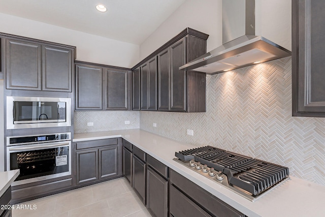 kitchen with appliances with stainless steel finishes, backsplash, wall chimney exhaust hood, dark brown cabinetry, and light tile patterned floors