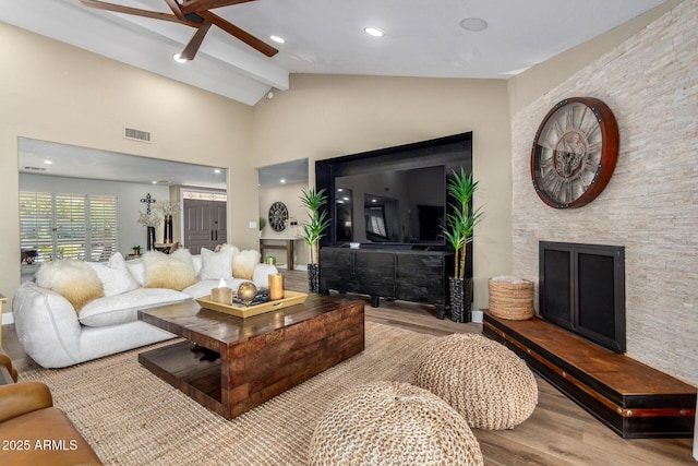 living area featuring a fireplace, visible vents, lofted ceiling with beams, a ceiling fan, and wood finished floors