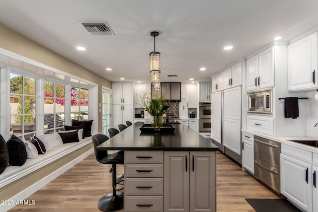 kitchen featuring a breakfast bar area, stainless steel appliances, visible vents, white cabinetry, and wood finished floors