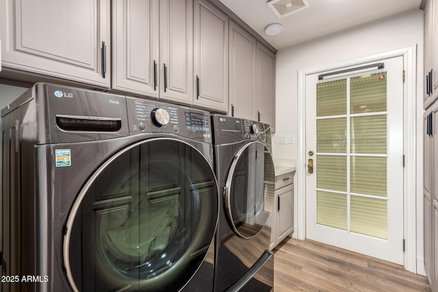 laundry area featuring light wood-type flooring, washing machine and dryer, cabinet space, and visible vents