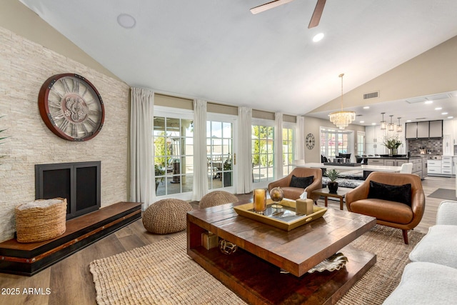 living room featuring light wood-type flooring, a fireplace, visible vents, and lofted ceiling