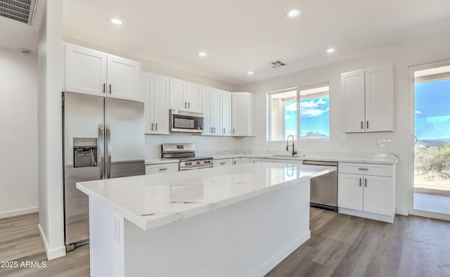 16025 E Rancho Laredo Dr, Scottsdale, AZ 85262 - kitchen with stainless steel appliances, a kitchen island, light wood finished floors, light stone counters, and white cabinets
