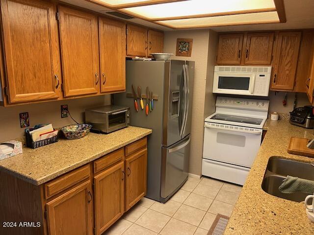 kitchen featuring light stone counters, white appliances, sink, and light tile patterned floors