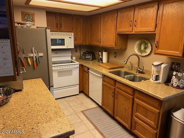 kitchen with stainless steel appliances, light tile patterned flooring, light stone countertops, and sink