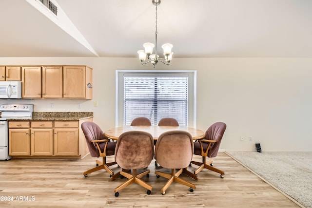 dining space with light wood-type flooring, an inviting chandelier, and vaulted ceiling