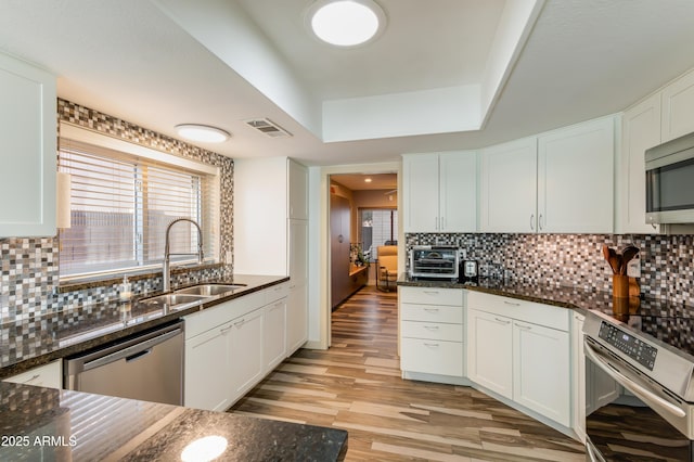 kitchen featuring stainless steel appliances, a sink, visible vents, backsplash, and dark stone counters