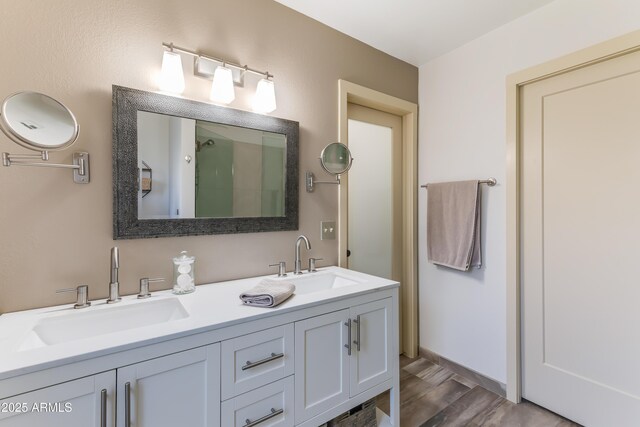 bathroom with an enclosed shower, double vanity, wood finished floors, and a sink