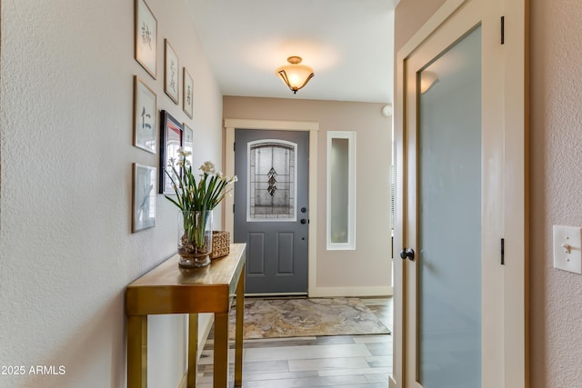 entryway featuring baseboards, wood finished floors, and a textured wall